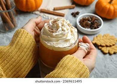 Woman holding cup of pumpkin spice latte with whipped cream at light grey table, closeup - Shutterstock ID 2369611495