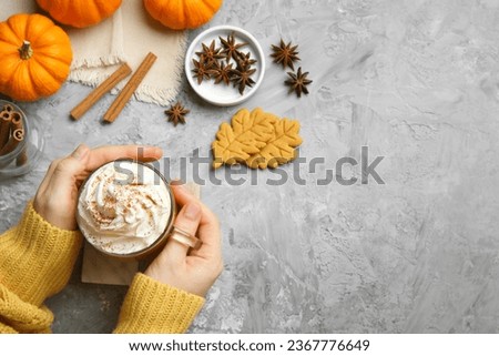 Woman holding cup of pumpkin spice latte with whipped cream at light grey table, top view. Space for text