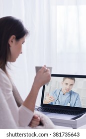 Woman Holding Cup, Sitting In Front Of Laptop Listening To Skype Doctor