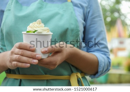 Woman holding cup with tasty frozen yogurt outdoors, closeup