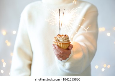 Woman holding cupcake with burning sparklers against blurred festive lights, closeup - Powered by Shutterstock