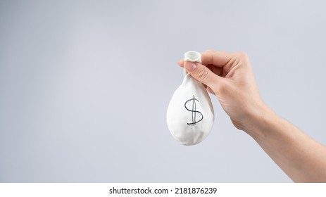 A Woman Is Holding A Deflated Balloon With A Dollar Sign. The Concept Of An Inflated Currency Value.