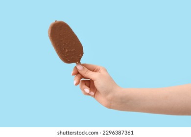 Woman holding delicious chocolate covered ice cream on stick against blue background