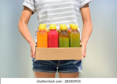 Woman holding delivery box of freshly cold pressed fruit and vegetable juice bottles. Closeup of female person carrying organic raw juices. Juicing is a food trend for diet cleanse detox.