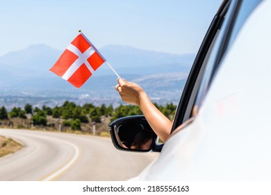 Woman holding Denmark flag from the open car window driving along the serpentine road in the mountains. Concept