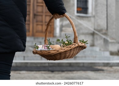 Woman holding Easter basket for blessing in a church. Traditional woven wicker Paschal basket filled with various food, ready to be blessed by a priest as part of the Easter tradition.