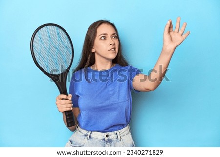 Woman holding an electric mosquito zapper in a blue studio.