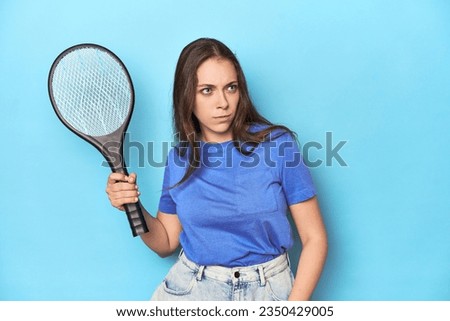Woman holding an electric mosquito zapper in a blue studio.