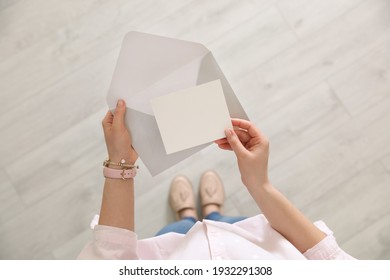 Woman holding envelope and blank greeting card indoors, top view