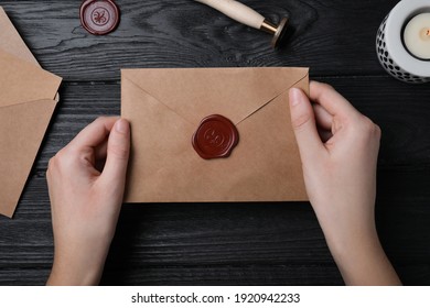 Woman Holding Envelope With Wax Seal At Black Wooden Table, Top View