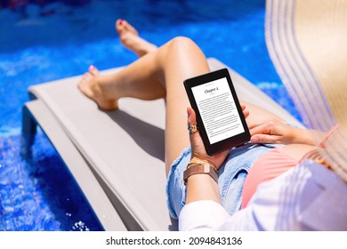 Woman holding e-reader device and reading e-book by the pool