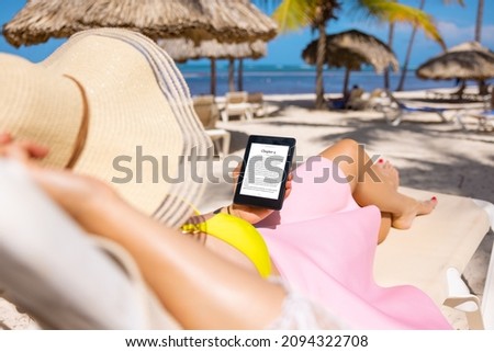 Woman holding e-reader device and reading e-book on the beach