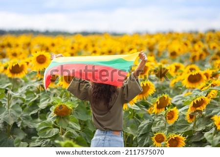Woman holding flag of Lithuania in a sunflowers field. Back view. Lithuanian Flag Day. Independence restoration Day. Travel and love Lithuania concept. Selective focus.