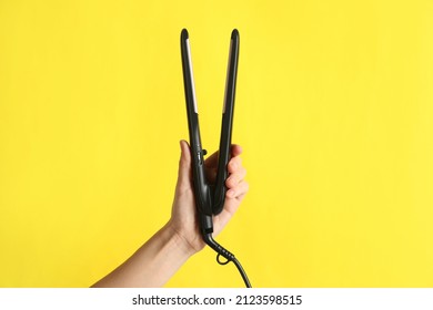 Woman Holding Flat Hair Iron On Yellow Background, Closeup