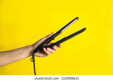 Woman Holding Flat Hair Iron On Yellow Background, Closeup