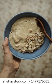 Woman Holding Flaxseed Porridge With Almonds And Coconut Milk In A Blue Bowl With Wooden Spoon. Overhead