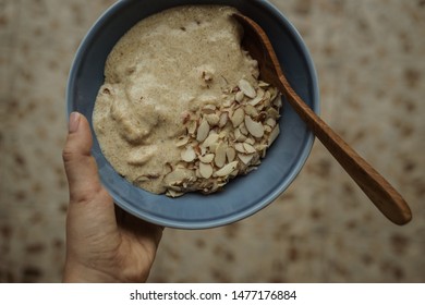 Woman Holding Flaxseed Porridge With Almonds And Coconut Milk In A Blue Bowl With Wooden Spoon. Overhead