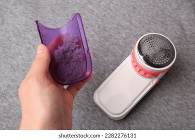 Woman holding fluff collector with lint of fabric shaver near light grey cloth, closeup - Shutterstock ID 2282276131