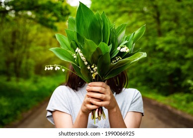 Woman holding fresh bouquet of lily of the valley flowers (Convallaria majalis) in forest. Spring flowers with green leaves, lilies of the valley in woman's hands