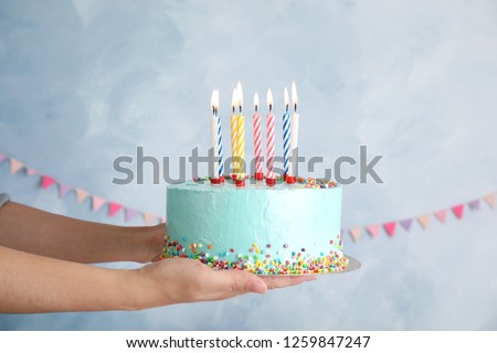 Woman holding fresh delicious birthday cake with candles on color background