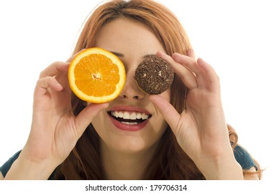 Woman holding in front of her eyes one orange and one candy,choosing between healthy and unhealthy food