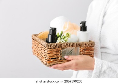 Woman Holding Gift Basket With Bath Supplies And Flowers On Light Background