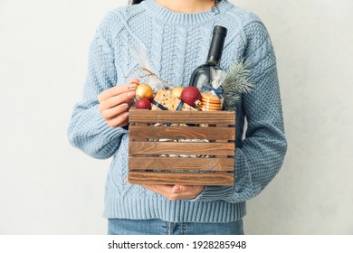 Woman Holding Gift Basket With Products On Light Background