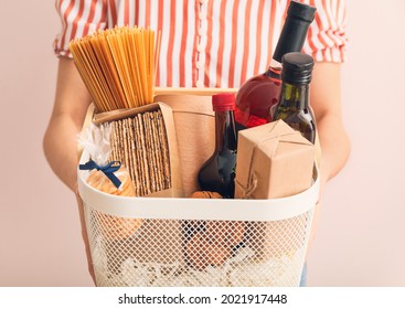 Woman Holding Gift Basket With Products On Color Background, Closeup