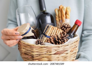 Woman holding gift basket with products and Christmas decor on light background