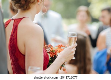 Woman Holding A Glass Of Champagne At A Summer Party. Party Outside With Chic Clothes. Bride With Red Wedding Dress At An Outdoor Wedding 