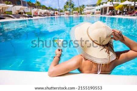 Woman holding glass of cocktail while relaxing in swimming pool in resort on vacation