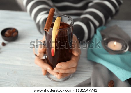 Woman holding glass cup of delicious mulled wine on wooden table, closeup