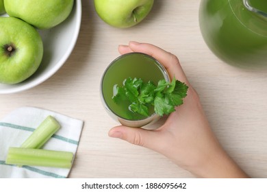 Woman Holding Glass Of Fresh Celery Juice At White Table, Top View