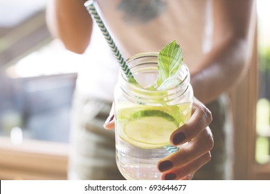 Woman holding glass of infused water with cucumber, lime and mint