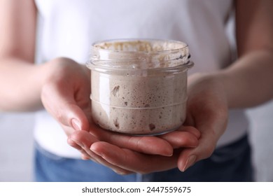 Woman holding glass jar with fresh sourdough starter, closeup