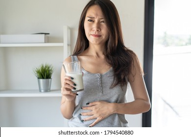 Woman holding a glass of milk and having a stomach ache from lactose intolerance.