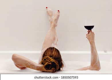 Woman Holding Glass With Red Wine And Lying In Bathroom Full Of Foam. Relaxing At Home