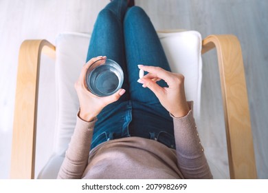 Woman holding glass of still water and taking painkiller from headache pain. Woman taking pills, antidepressant or antibiotic medication - Shutterstock ID 2079982699