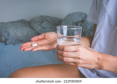 Woman holding glass of still water and taking painkiller from headache pain. Woman taking pills or antidepressant - Shutterstock ID 2129305859