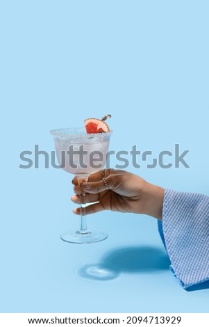 Woman holding glass of tasty grapefruit margarita on color background