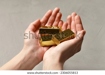 Woman holding gold bars against grey textured background, closeup