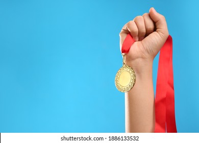 Woman holding gold medal on light blue background, closeup. Space for text - Powered by Shutterstock