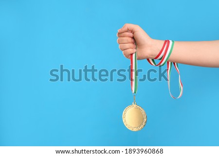 Woman holding gold medal on light blue background, closeup. Space for text