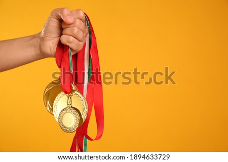 Woman holding gold medals on yellow background, closeup. Space for text