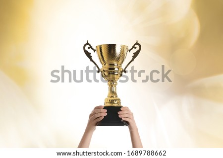 Woman holding gold trophy cup on color background, closeup