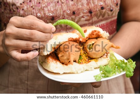Woman holding green chilli, Vada Pav/paav in her hand  usually served with sauce. Indian fast/street food snack, North India, Maharashtra.  vada sandwiched between two slices/lloaf of bread.