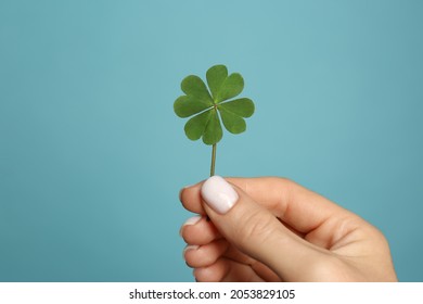 Woman holding green four leaf clover on light blue background, closeup
