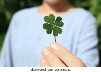 Woman holding green four leaf clover outdoors, closeup