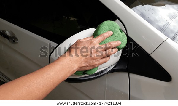 A
woman holding a green sponge to wash the car glass
