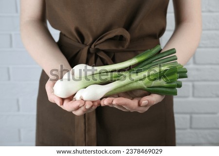 Woman holding green spring onions near white brick wall, closeup